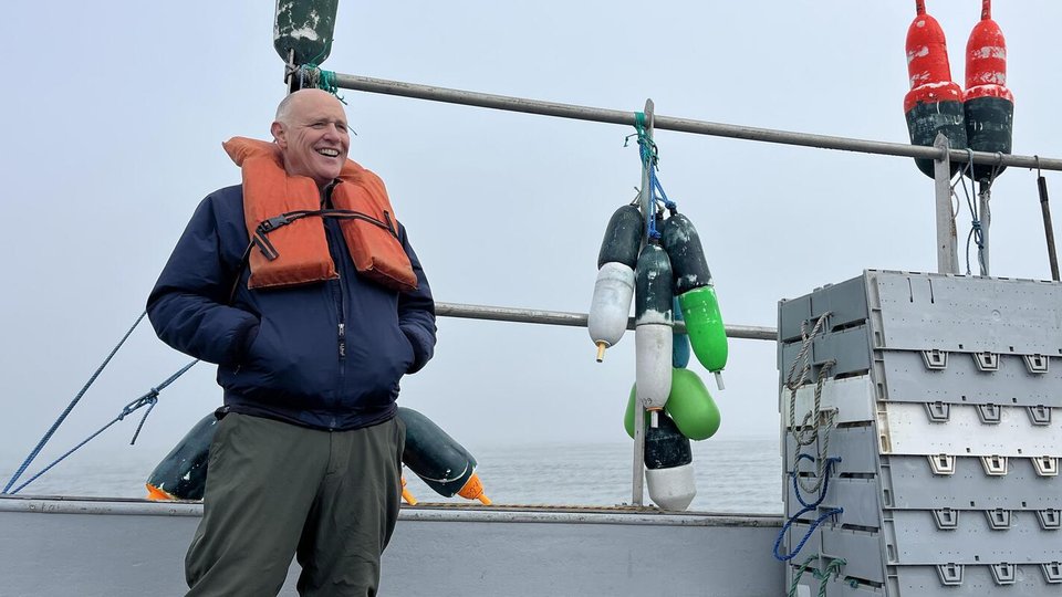 Paul Dobbins stands on Brent Nappi's boat. His hands are in his pockets and he smiles.