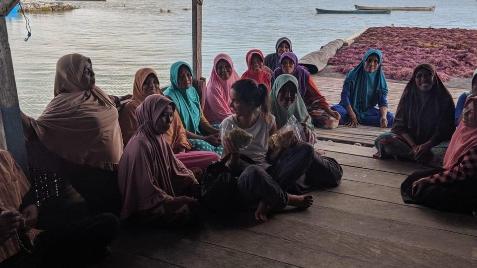 Shauna Mahajan sits in the middle of a group of women wearing colorful head wear on a dock on the water.