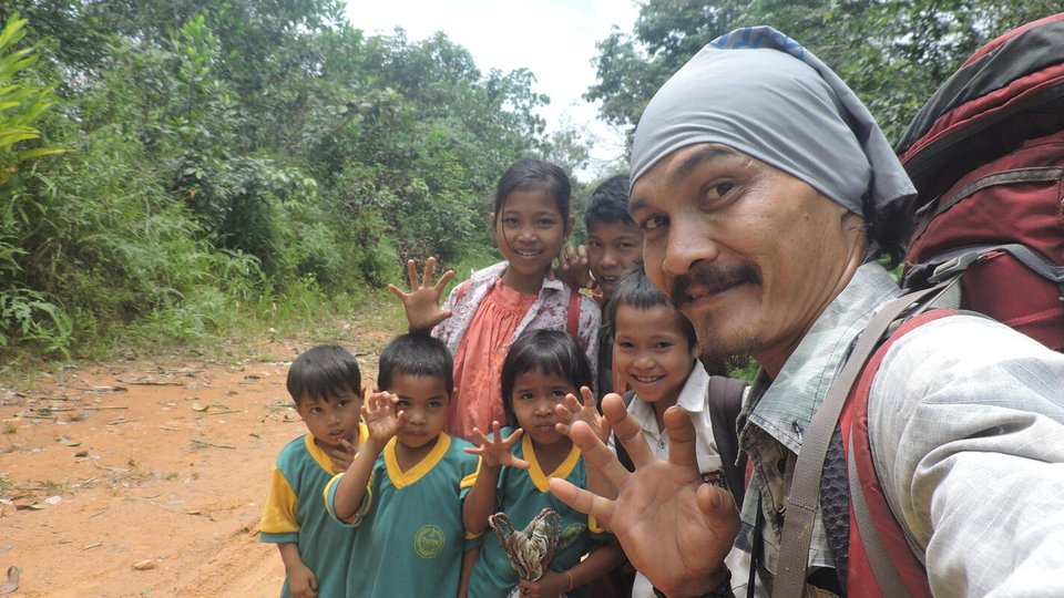 Man with red backpack stands on a forest path with group of children all waving at the camera