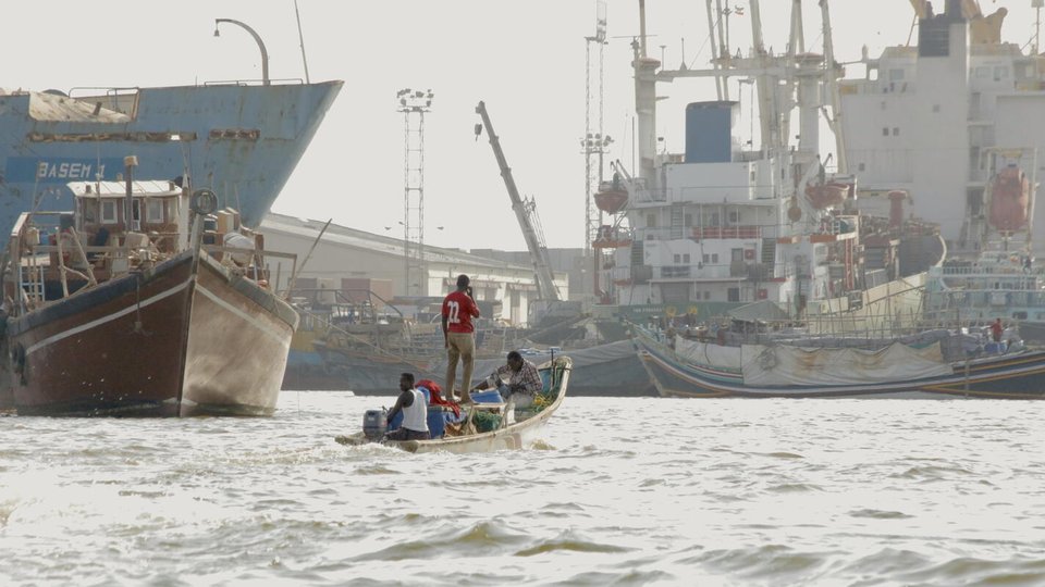 A small boat with three people on it travels between very large vessels