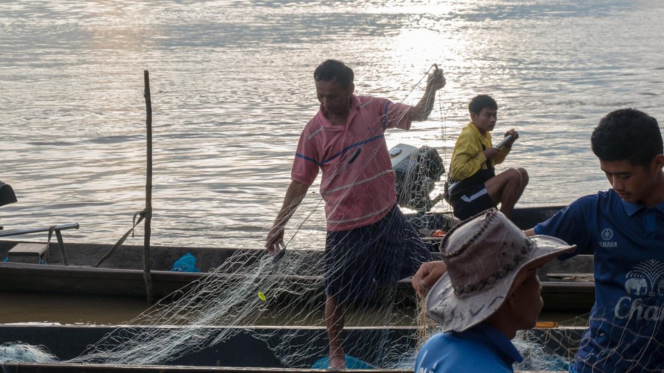 A group of fishermen repairing their nets while on their boats out on the water