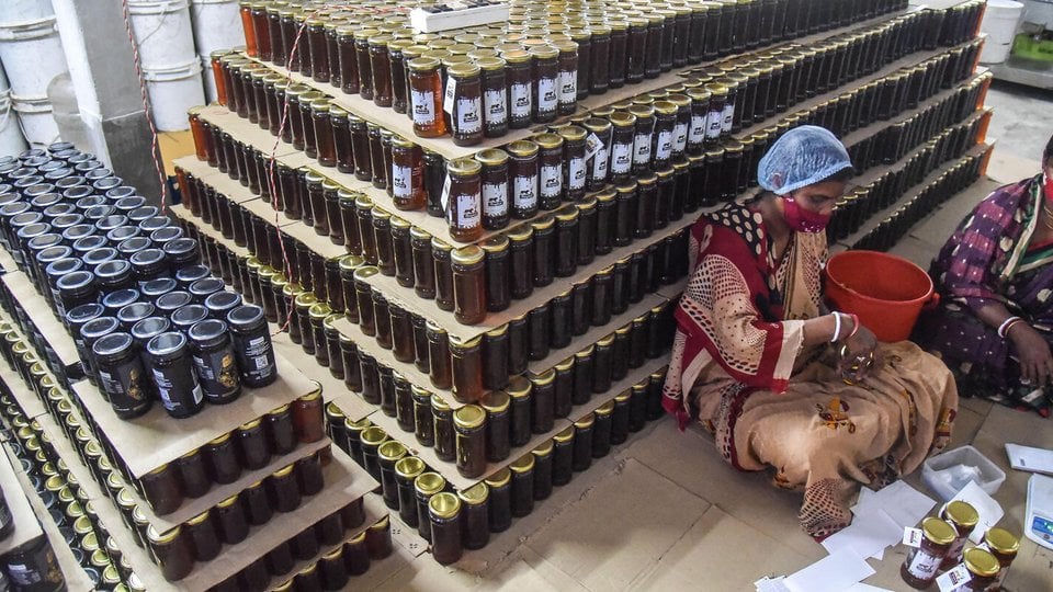Women sit in front of a large stack of full honey jars ready for shipment