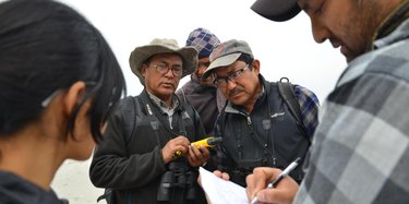 A man writes in a notebook while a group of people stand and observe