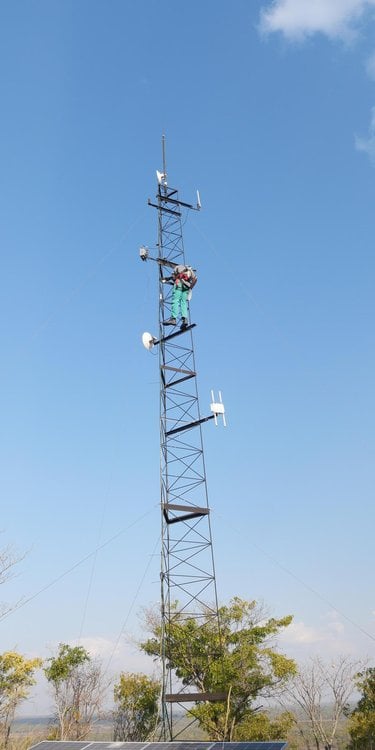A person stands high up on a tower with a bright blue sky in the background