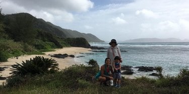 Ellie Yanagisawa kneels next to her nephew. Her grandma stands behind them. They all are on a beach in Amami.