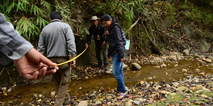 A group of people use a long yellow measuring tape to place a camera trap