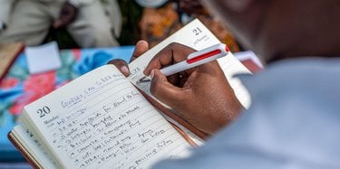 Close up of a person's hand writing notes in a notebook outside