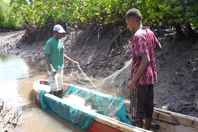 Two men stand in a small canoe on the shore, preparing nets