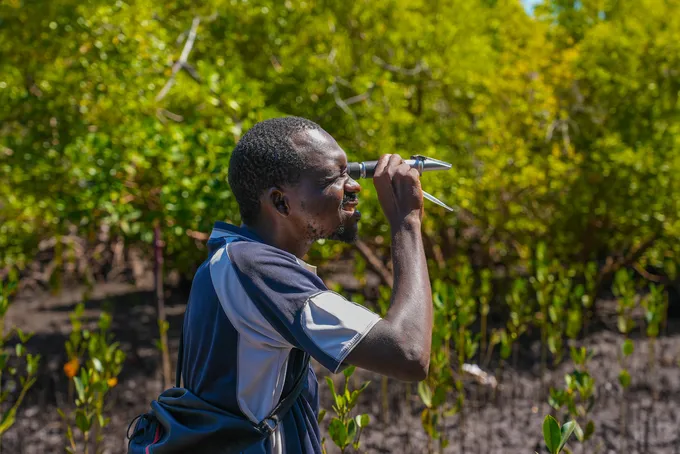 A man standing in a forested area, looking through binoculars