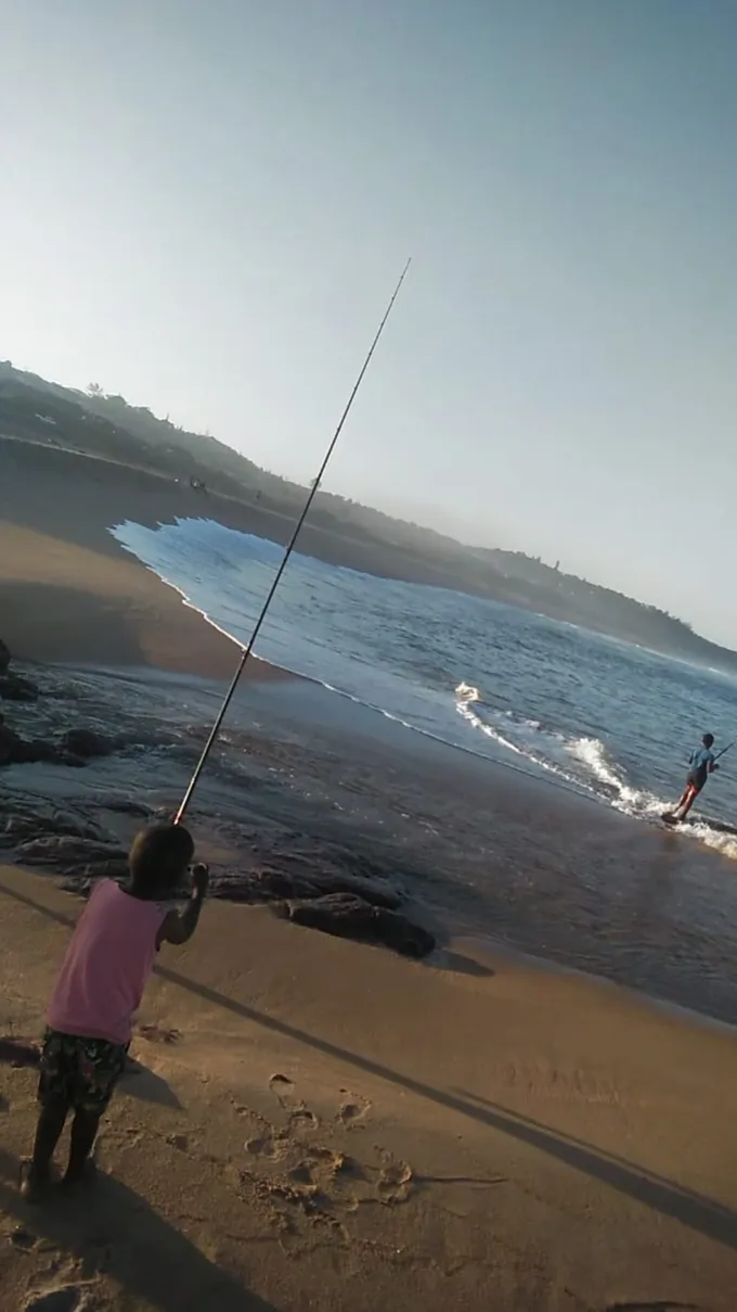 A boy with a long fishing pole casts into the surf