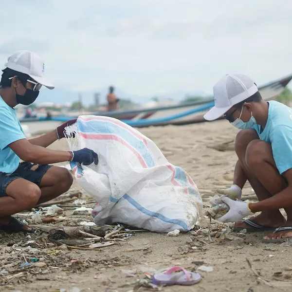 Two people in masks and gloves pick up waste on a beach