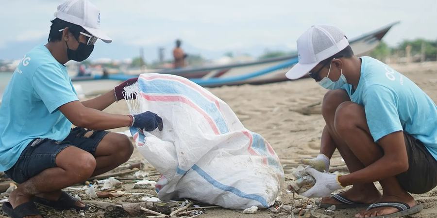 Two people in masks and gloves pick up waste on a beach