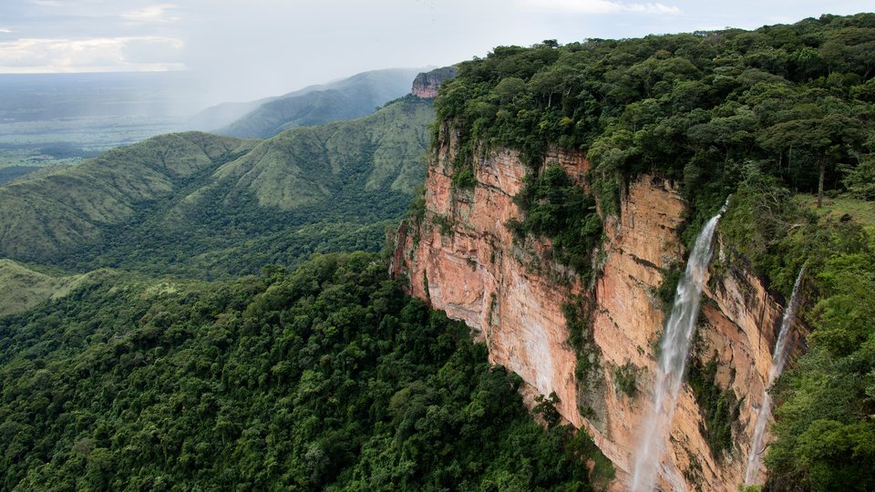 A waterfall cascades off a cliff with a lush green background