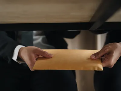 Two hands passing an envelope under table