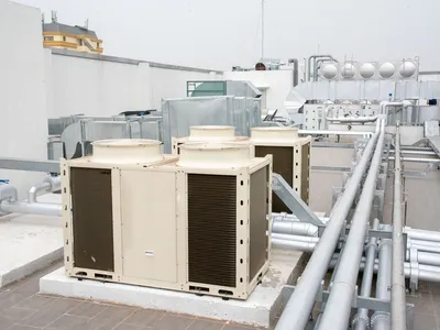 Industrial metal boxes sit on a roof with a number of long pipes