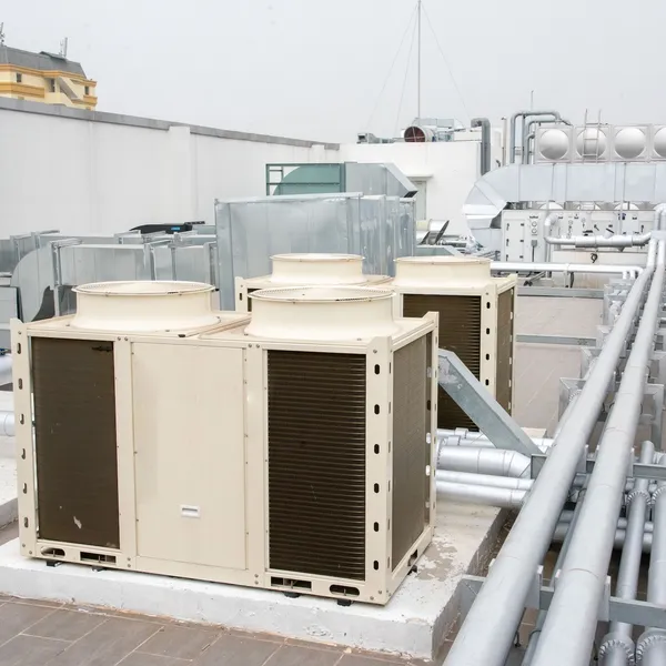 Industrial metal boxes sit on a roof with a number of long pipes