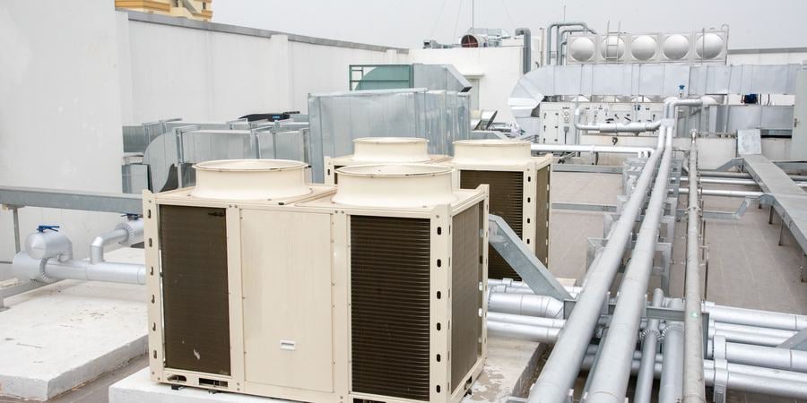 Industrial metal boxes sit on a roof with a number of long pipes