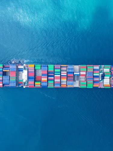 Aerial view looking down at a cargo vessel ship carrying hundreds of containers across the open ocean.