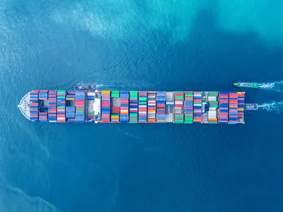 Aerial view looking down at a cargo vessel ship carrying hundreds of containers across the open ocean.
