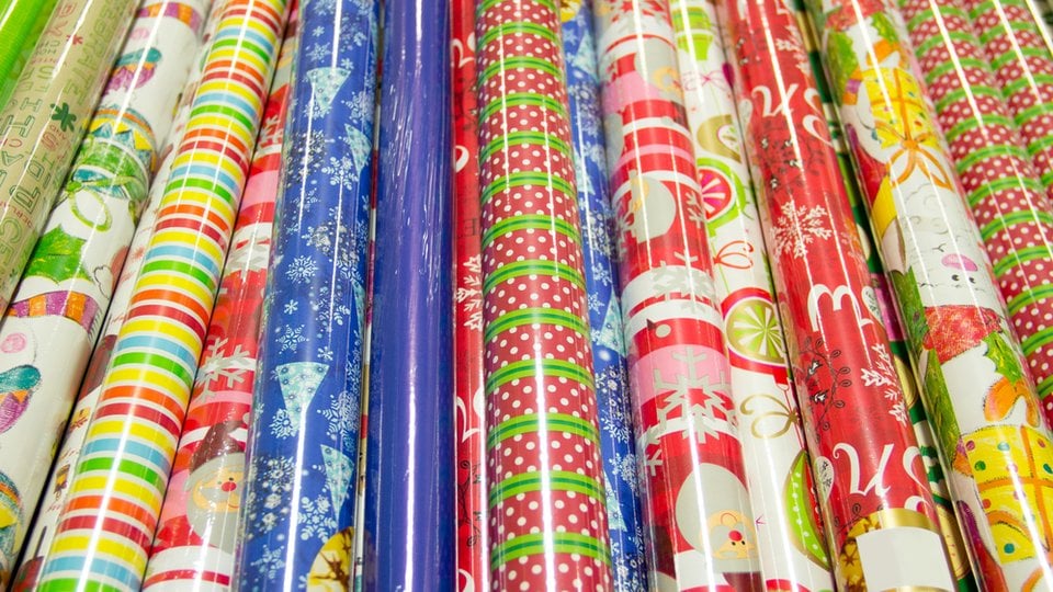 Dozen holiday and Christmas wrapping paper rolls of various colors and patterns