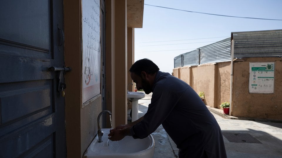 A man washes his hands in a sink outside a building