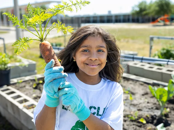 A student gardener holds up a large carrot