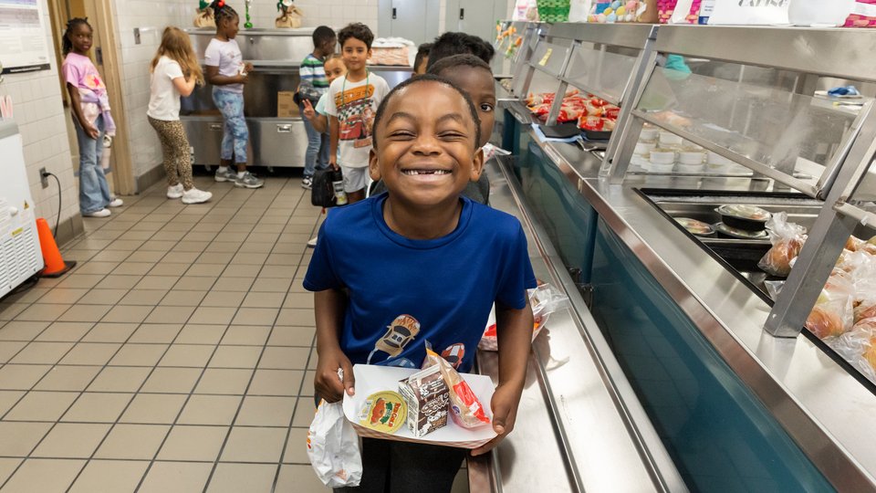A student grinning at the photographer from the cafeteria lunch line