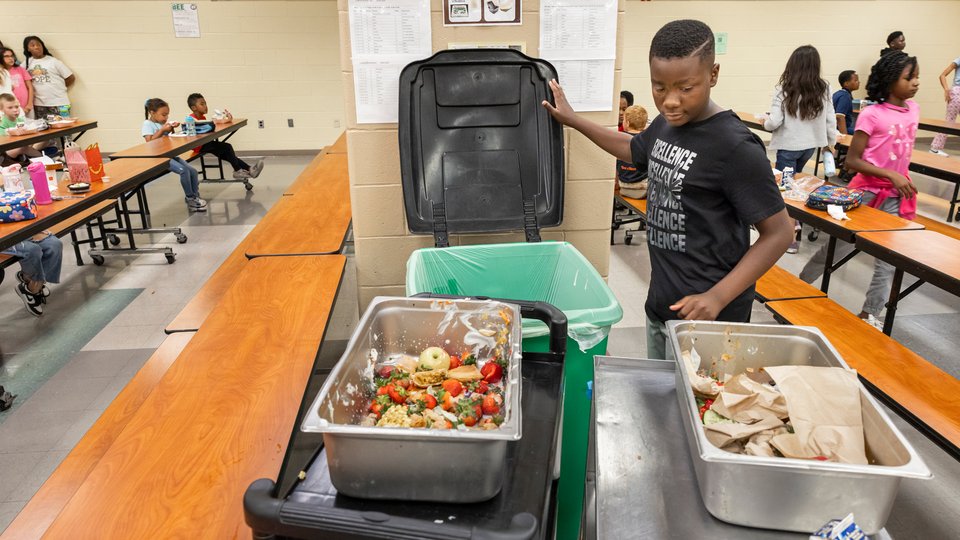In a school cafeteria, a student collects unfinished food in a bin
