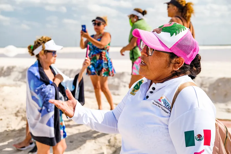 Five women in beach attire and hats standing on a sandy surface.