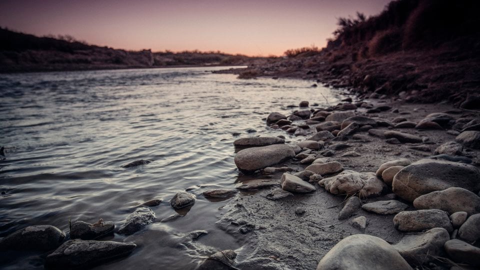A photo showing a rocky riverbank with gray water lapping against the shore.