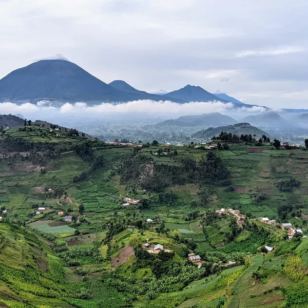 Rolling green hills with homes on them and large cloud-covered mountains in the background