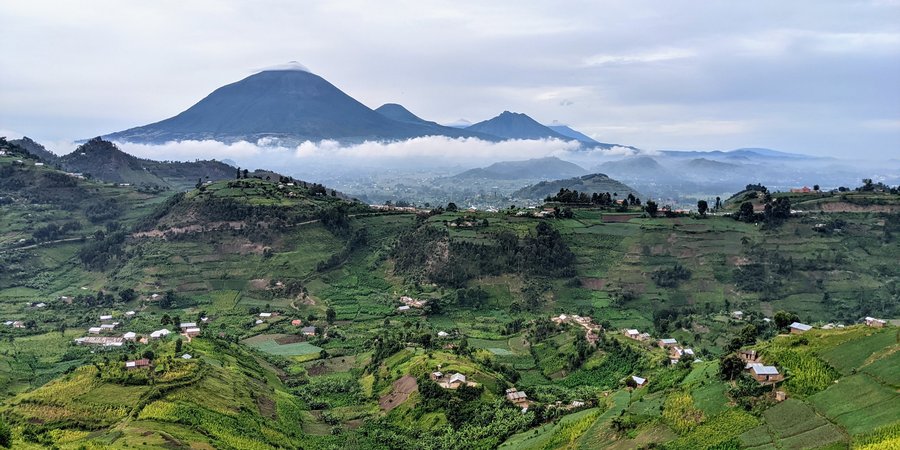 Rolling green hills with homes on them and large cloud-covered mountains in the background