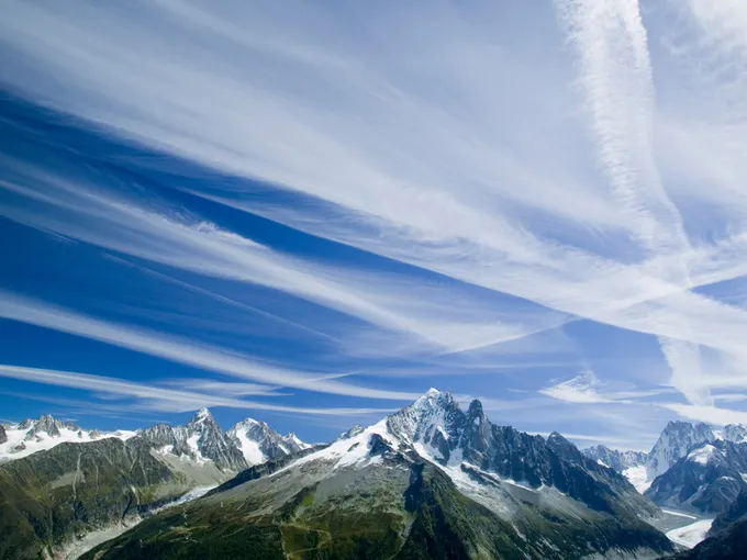 Tall mountains with blue sky above. White vapor trails streak across the blue sky.