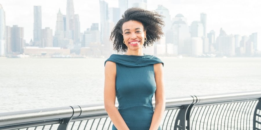 Alexa White stands in front of a river and city skyline smiling at the camera