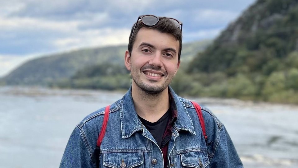 Alexander Nicolas stands in front of a lake and mountains