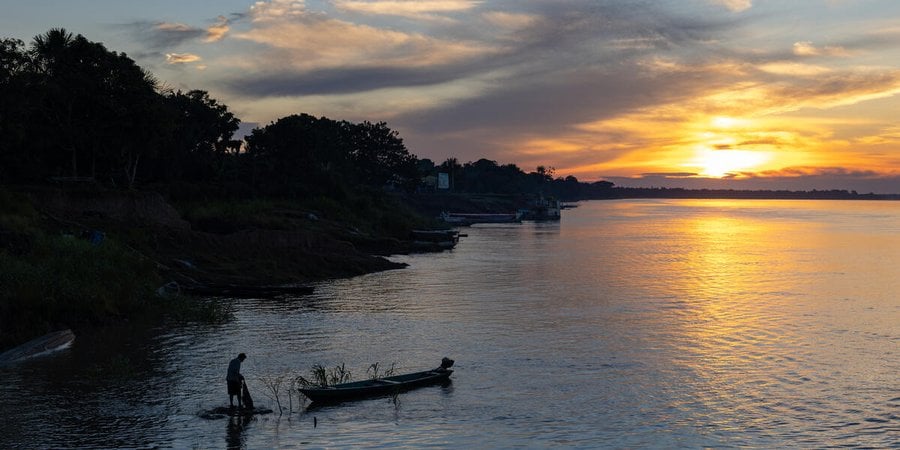 Sunset over water with a person in a canoe pulling a fishing net