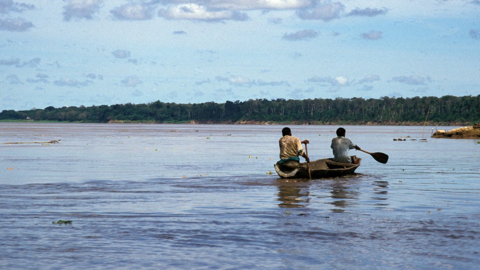 Two men paddle away in a small boat in the middle of the Amazon River.