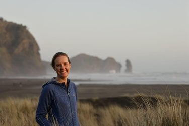 Annie Lewin stands on the coast with the ocean and rocks behind her.