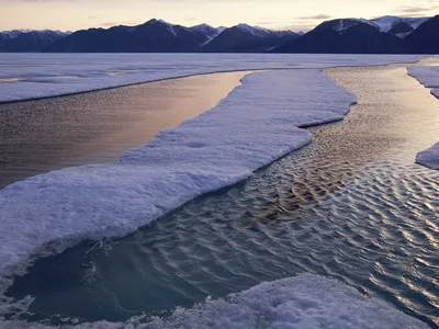 Frozen body of water with mountains in the background. There are a few areas where the water has not frozen.