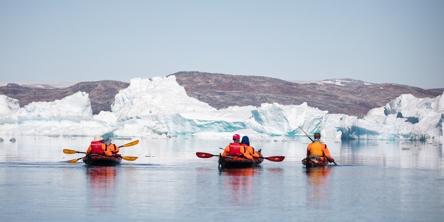 Kayakers in orange gear view glacier edge