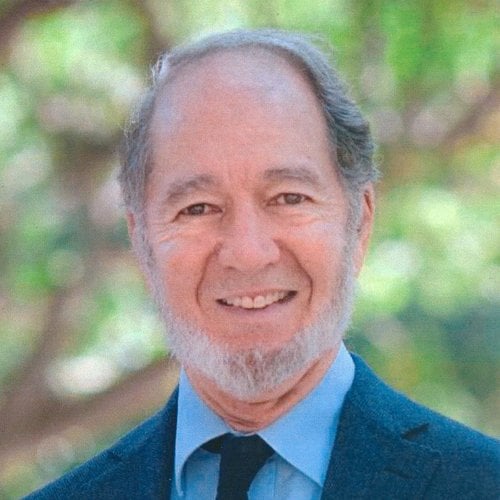 Jared Diamond smiles at the camera, wearing a suit against a tree background