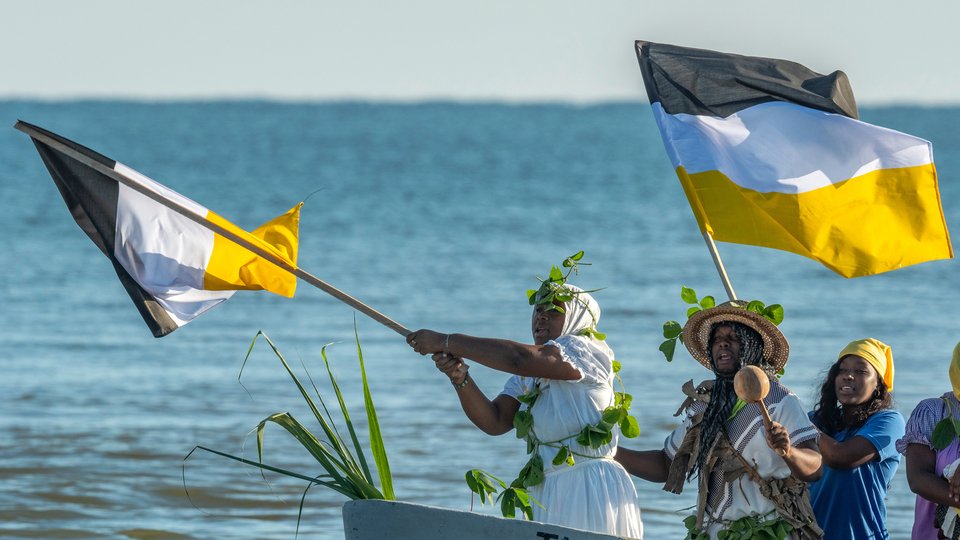 A group of celebrants, a waving the Garifuna flag, reenact their ancestors’ arrival