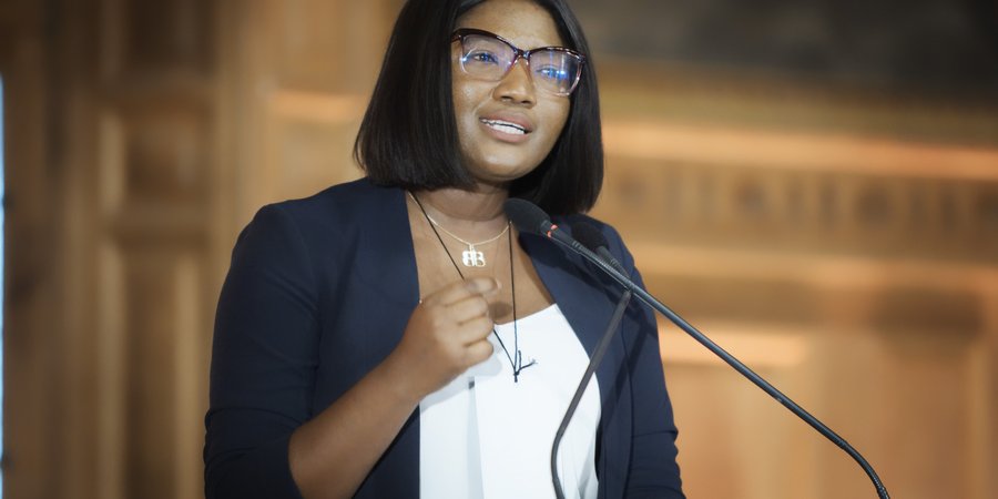 Betty Osei Bonsup stands at a lectern giving a speech in a blue blazer and white shirt