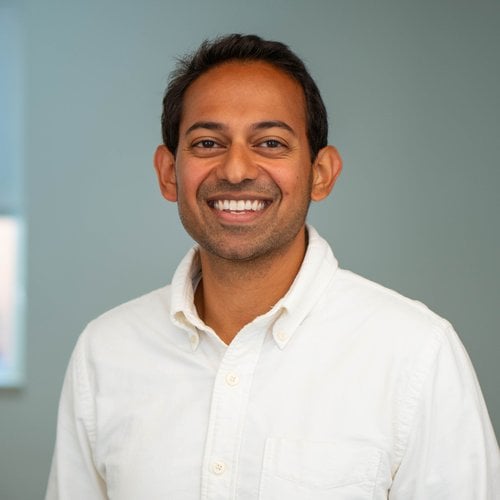 A headshot of a smiling man in a button down shirt