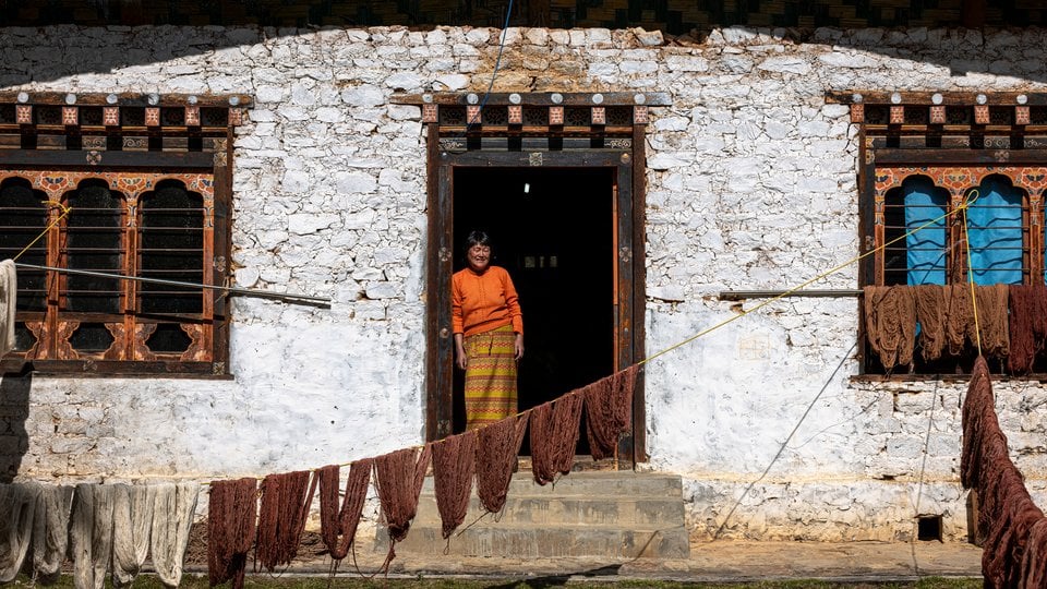A woman standing in the doorway of a white house with fibers drying on a line outside