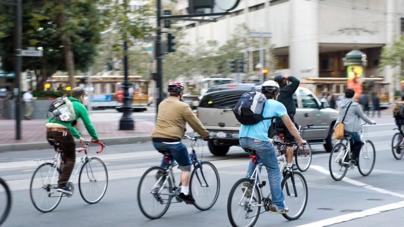 Commuters bike to work in city Environmentally conscious bikers cycling in traffic in San Francisco, California, United States
