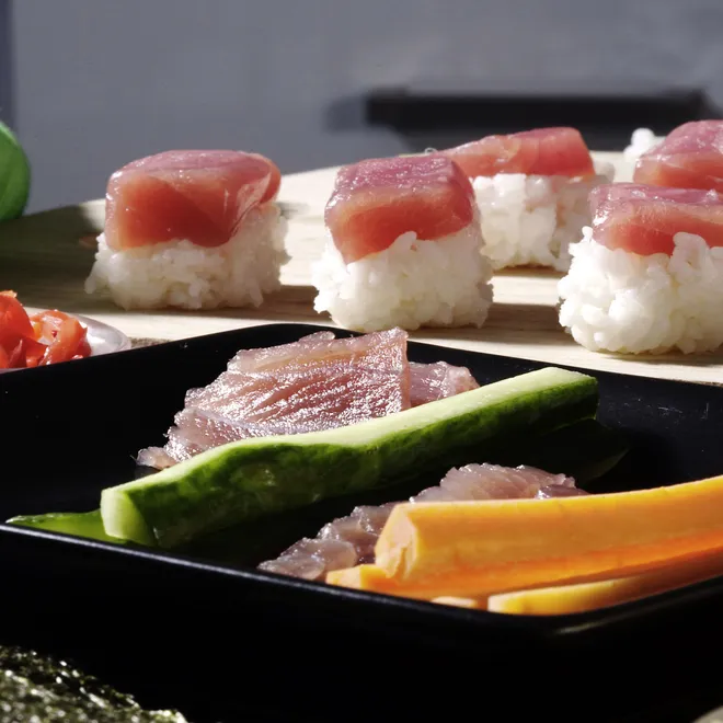 A photo of a dark tray holding sushi, sashimi and vegetables.