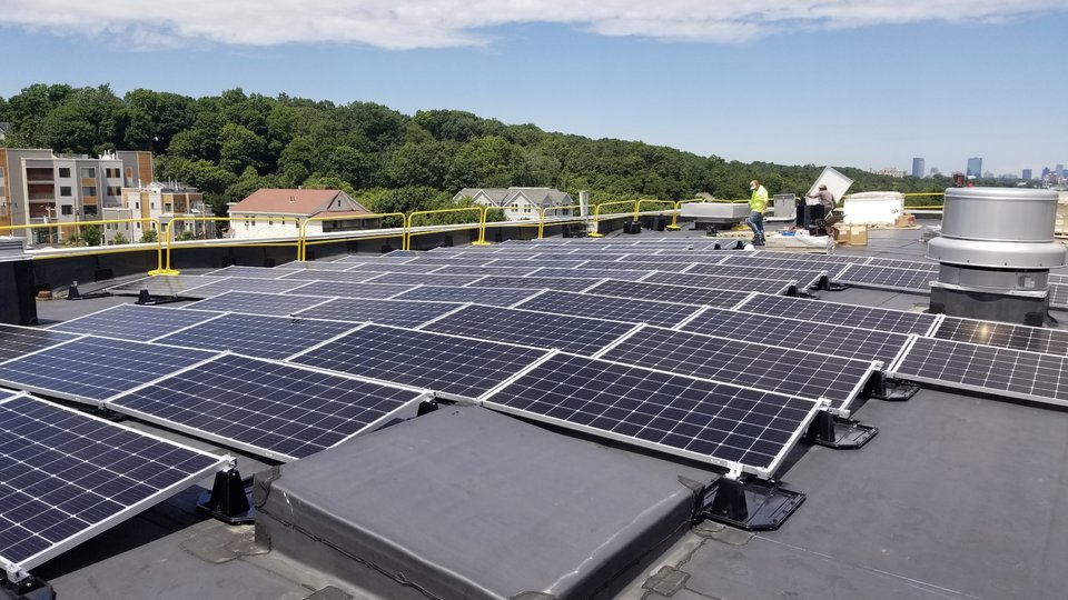 Workers install solar panels on a rooftop in Boston, MA.