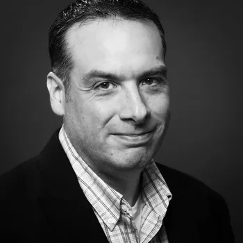 A black and white headshot of Brent smiling at the camera.