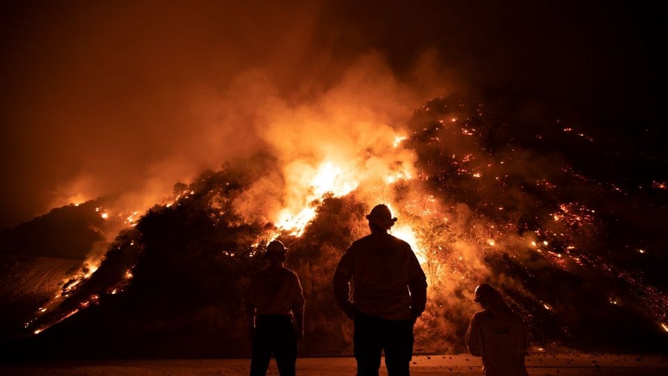 Firefighters fight a large fire burning in the hills.